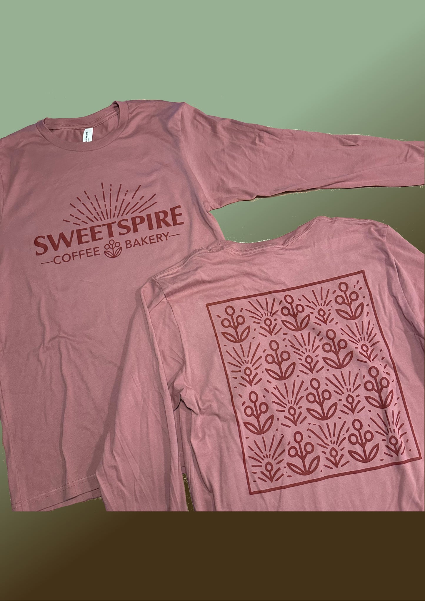 Pink long-sleeve shirt with 'Sweetspire Coffee Bakery' logo on front and flower pattern on back against a green background